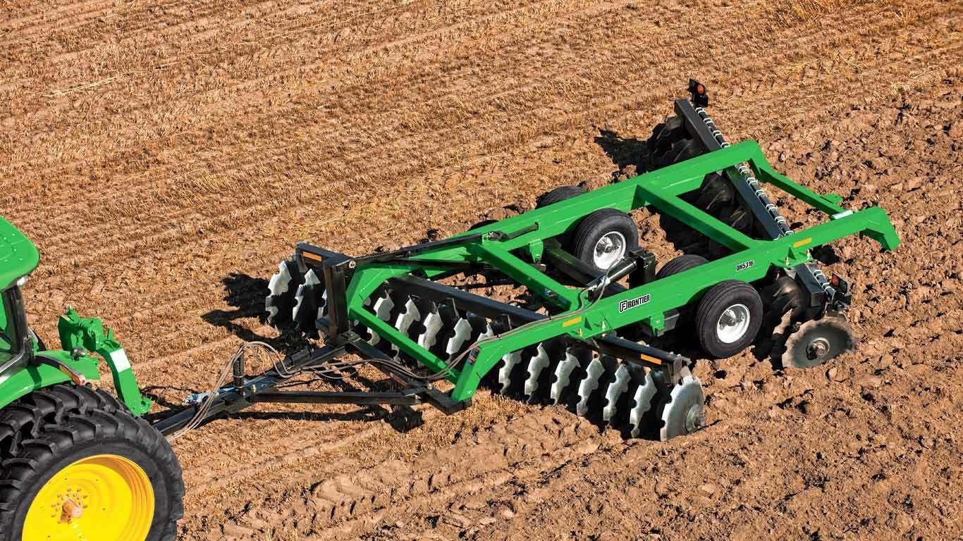 Green tractor pulling a Frontier DH53 series offset disk in a field.