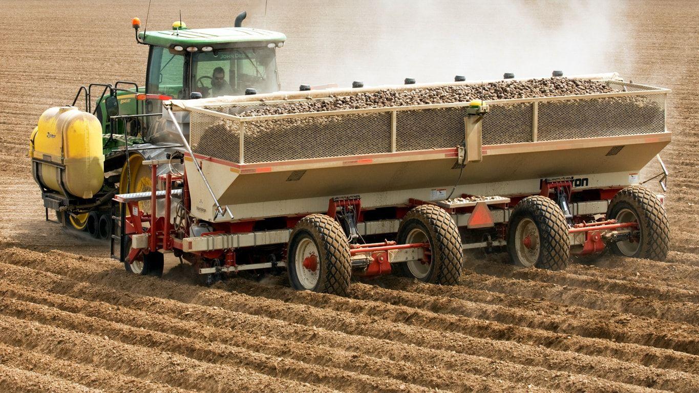 Tractor pulling a large potato planter in a field, planting rows of potatoes.